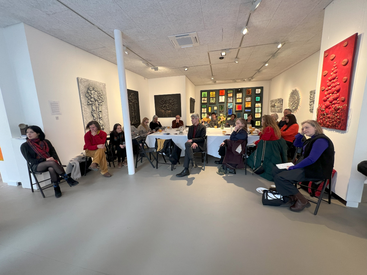 A group of people sitting around a table in a room painted white with artworks on the wall.