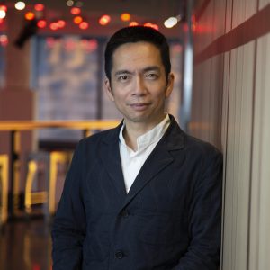 A photo of a man seen from the waist up and wearing a black jacket and white shirt