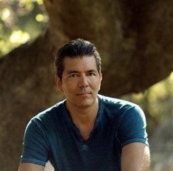 A photo of a man with dark hair wearing a blue t-shirt
