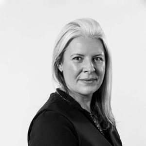 A black and white photo of a woman looking towards the camera wearing a dark jacket.